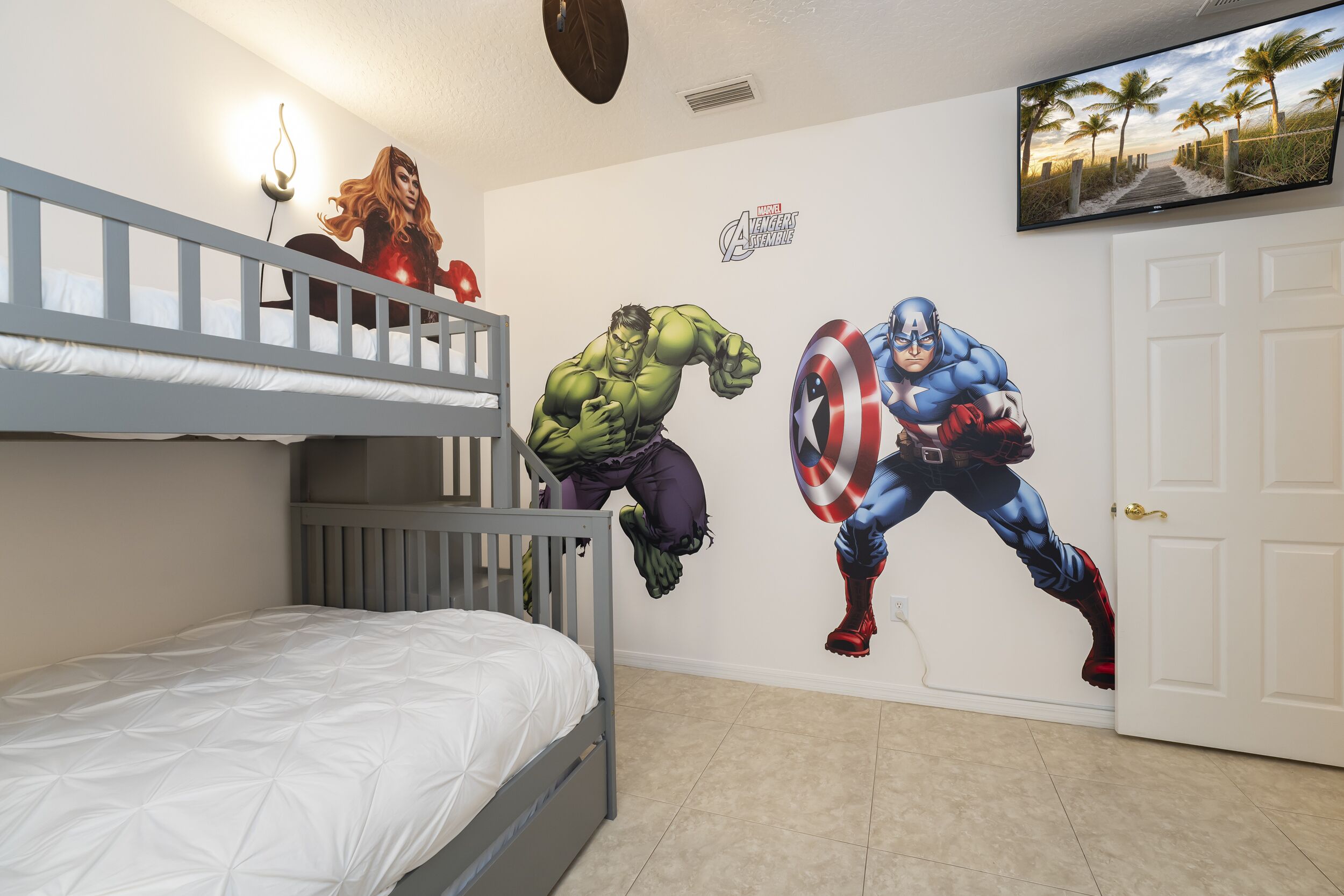 Une chambre avec un lit superposé, une fresque murale représentant des personnages des Avengers, une télévision et une porte.