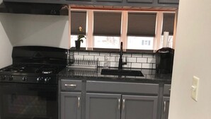Uma cozinha com armários cinza, um fogão preto, uma pia e uma janela com persianas.