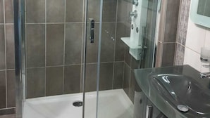 Et moderne badeværelse med et glasafskærmet brusebad, et vaskeskab med håndvask og et spejl.