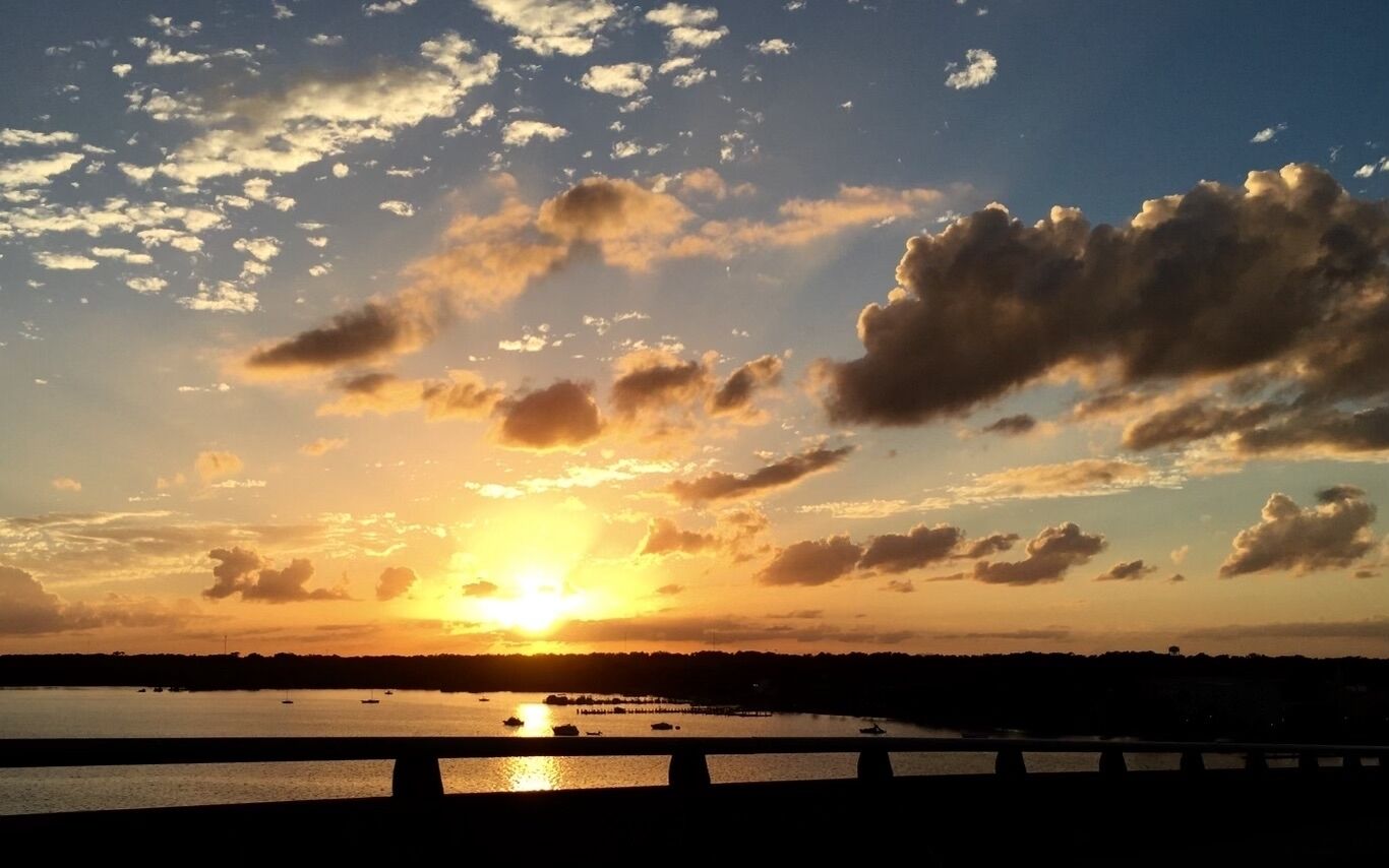 A sunset over a body of water with boats and a bridge in the foreground.