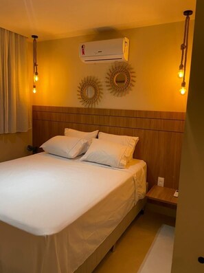 A hotel room with a bed, a wall-mounted air conditioner, and two wall sconces.