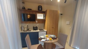 A compact hotel room with a kitchenette, a dining area with two chairs, and a bed. - Pipa Day Flats (Tibau do Sul)