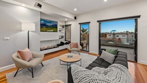 A modern living room with a sofa, armchair, and coffee table, a fireplace, and a city view through large windows. - StayCentral - Moonee Ponds Penthouse (Moonee Ponds)