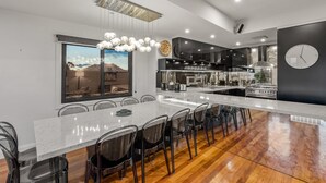 A modern kitchen with a large island, stainless steel appliances, and a dining area with chairs. - StayCentral - Moonee Ponds Penthouse (Moonee Ponds)