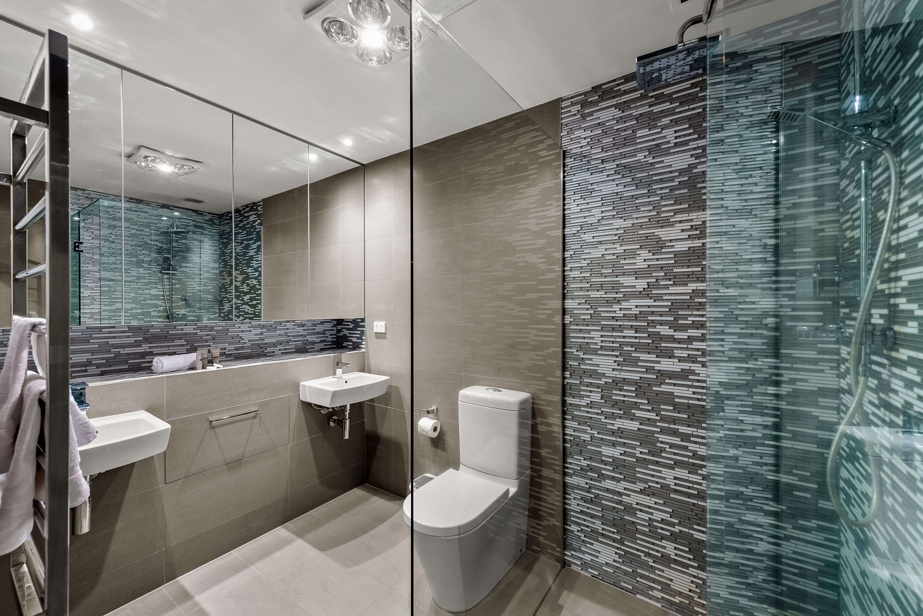 A modern bathroom with a glass shower enclosure, a toilet, and a vanity with a mirror.