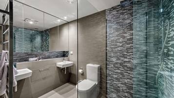 A modern bathroom with a glass shower enclosure, a toilet, and a vanity with a mirror.