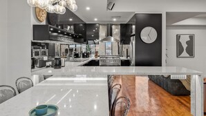 A modern kitchen with a central island, stainless steel appliances, and a large clock on the wall. - StayCentral - Moonee Ponds Penthouse (Moonee Ponds)