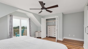 Een slaapkamer met een groot bed, een plafondventilator, een houten vloer, een dressoir en een kast.