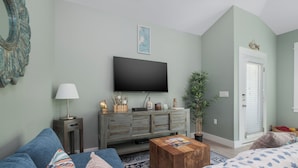 Ein Wohnzimmer mit Flachbildfernseher, Couchtisch aus Holz, blauem Sofa und einer Kommode mit Dekoration.