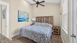 A bedroom with a bed, a ceiling fan, a nightstand, a lamp, and a window with blinds. - 1385 - Stay Awhile - Cozy Corolla Getaway Near Beach & Community Pool (Corolla)