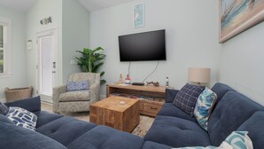 Una sala de estar con un sofá, una mesa de centro, un televisor montado en la pared y una mesita de noche con una lámpara.