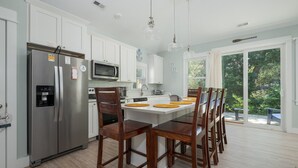 A modern kitchen with white cabinets, stainless steel appliances, and a central island with wooden chairs. - 1385 - Stay Awhile - Cozy Corolla Getaway Near Beach & Community Pool (Corolla)
