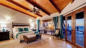 Ein Schlafzimmer mit Bett, Nachttisch, Deckenventilator und Meerblick durch eine Schiebetür.