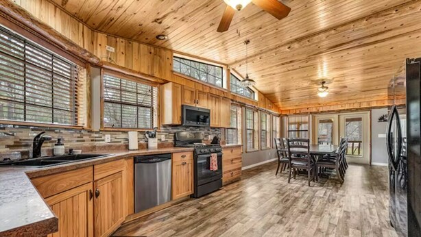A spacious kitchen with wooden cabinets, a large island, and a dining area with a table and chairs. - Incredible Rustic Lakeside Cabin in the Woods! Near Lakes, Skiing and Trails! (Lakeside)