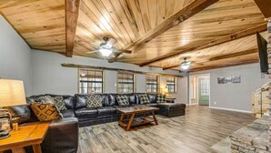 A spacious living room with a wooden ceiling, a black leather sofa, a wooden coffee table, and a stone fireplace. - Incredible Rustic Lakeside Cabin in the Woods! Near Lakes, Skiing and Trails! (Lakeside)