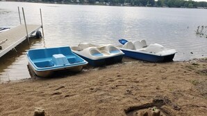 Ein sandiger Strand mit drei Tretbooten und einem Steg.