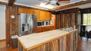 Eine rustikale Küche mit Holzschränken, einem Edelstahlkühlschrank, einer Holzausziehtafel und einem Deckenventilator.