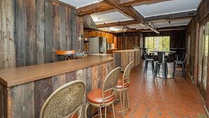 Ein rustikales Interieur mit freiliegenden Holzbalken, einer Bar mit Hockern und einer Küche im Hintergrund.