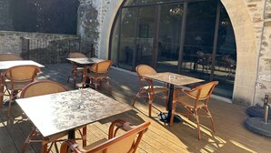An outdoor patio with stone walls, large arched windows, and wicker furniture. - Domaine du Prieuré d'Estagel (Saint-Gilles)