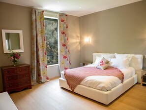 Une chambre à coucher avec un lit, une commode, un miroir et une fenêtre avec des rideaux.