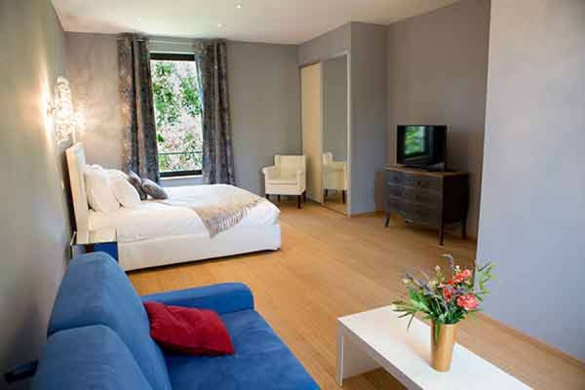Een moderne slaapkamer met een bed, een blauwe bank, een televisie en een kleine tafel met een bloevas.