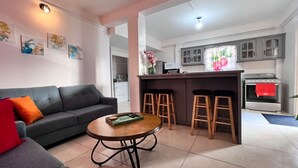 Un soggiorno moderno con divano, tavolino da caffè e angolo cottura con piano cottura e sgabelli da bar.