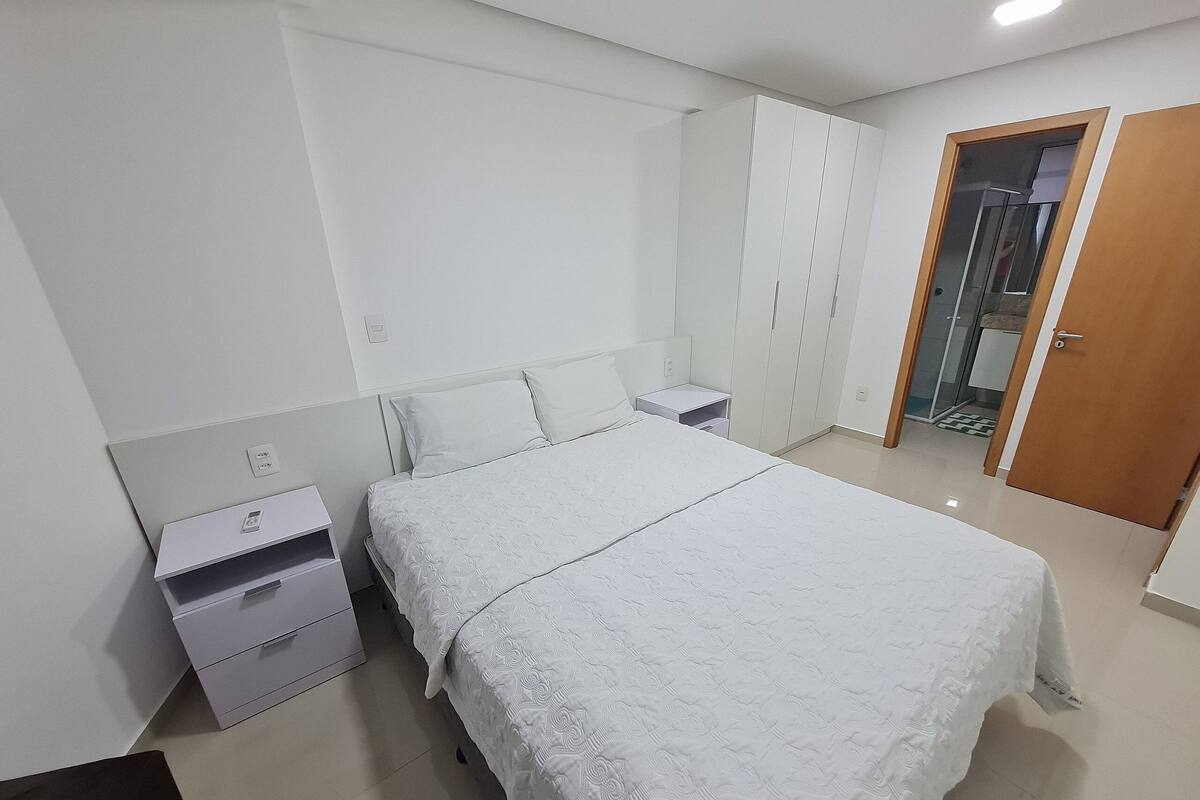 A bedroom with a large bed, a wardrobe, a nightstand, and a bathroom visible through an open door.