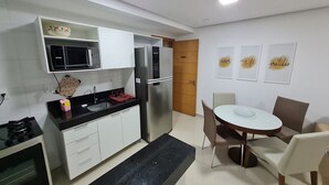 Una cocina moderna con armarios blancos, un refrigerador de acero inoxidable, un microondas y una estufa a gas. Hay una mesa de comedor con sillas y una alfombra pequeña.