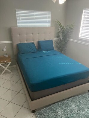 Un dormitorio con una cama, una mesita de noche, una lámpara y una planta en maceta.