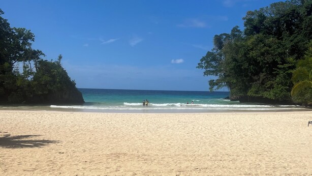 A beach with clear blue water, sandy shore, and dense green foliage on either side. - Relaxing 3 bedroom pool home (Miami)