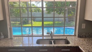 A kitchen with a large window overlooking a swimming pool, wooden cabinets, and a built-in sink. - Relaxing 3 bedroom pool home (Miami)