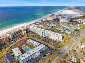 Ett flygbildsfoto av ett hotellkomplex vid kusten, med flera byggnader, en strand och en stor parkeringsplats.
