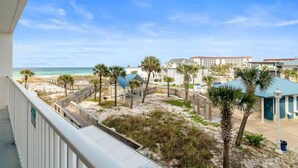 A beach view from a balcony, palm trees, a beach pavilion, and a hotel building. - Seacrest Beachfront 2BR | Angled Gulf View + Pools (Fort Walton Beach)