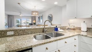 A modern kitchen with granite countertops, stainless steel sink, white cabinetry, and pendant lighting. - Seacrest Beachfront 2BR | Angled Gulf View + Pools (Fort Walton Beach)