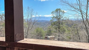 Une vue depuis une fenêtre donnant sur un paysage montagneux, avec des arbres et un ciel dégagé.