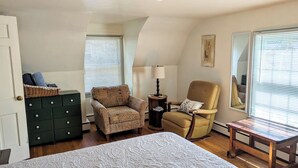 A bedroom with a bed, two armchairs, a small table, a lamp, a dresser, and a window with blinds. - Charming 2BR Private Home in Downtown Bellefonte • Near Penn State & I-80 (Bellefonte)