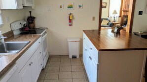 A compact kitchen with white cabinetry, a granite countertop, a white trash bin, and a fire extinguisher on the wall. - Charming 2BR Private Home in Downtown Bellefonte • Near Penn State & I-80 (Bellefonte)