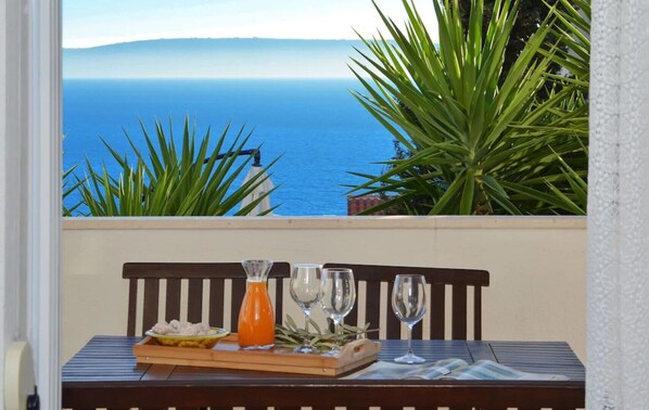 A table with a bottle of orange juice, two glasses, and a plate with food, overlooking a coastal view with green plants and a bench. - Wonderful quiet beach location 5 km from Trogir, swimming pool, sea view (Okrug Gornji)