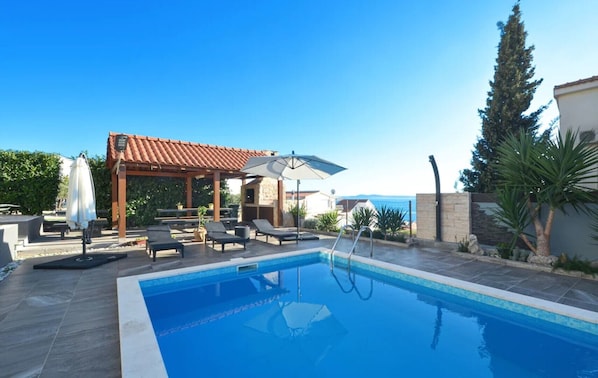Une piscine avec des chaises longues et des parasols, une pergola et une vue sur la mer.