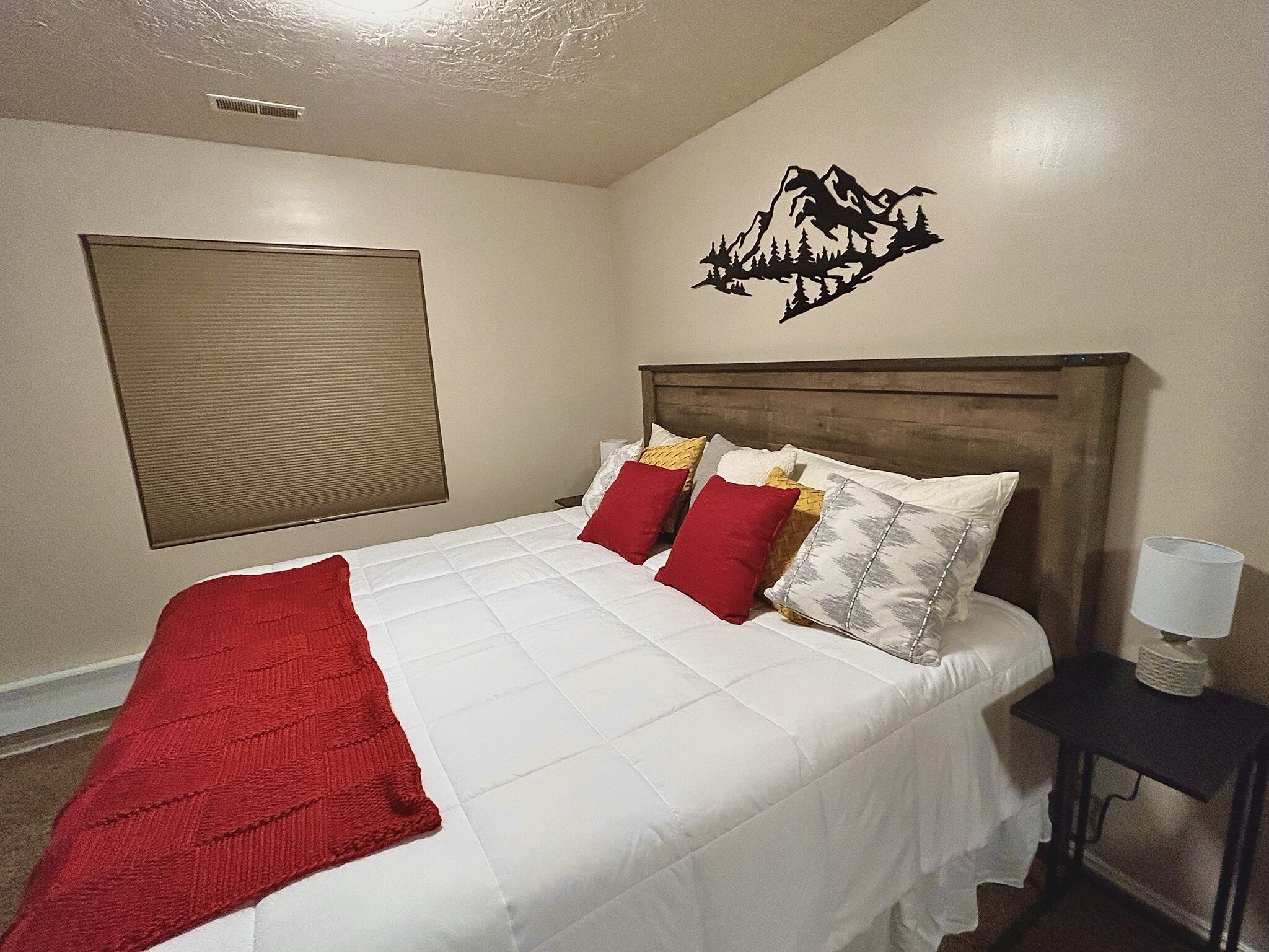 Un dormitorio con cama, cabecera, decoración en la pared, mesita de noche y lámpara.