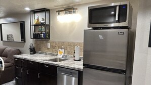 Een compacte keuken met een roestvrijstalen koelkast, een magnetron, een vaatwasser en een granieten aanrecht.
