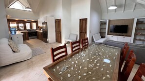 Een ruime woonkamer met een eettafel vol met schelpen, een keuken met moderne apparatuur en een grote flatscreen televisie aan de muur.
