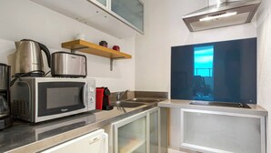 A modern kitchen with a microwave, toaster, kettle, and a coffee maker. There is a window with a view of the sky and a shelf with jars. - Studio Roche Ronde - Welkeys (Biarritz)