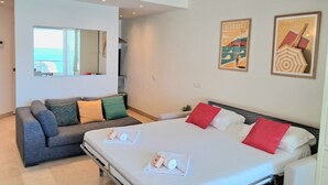 A modern hotel room with a large bed, a sofa, a small table, and a mirror. - Studio Roche Ronde - Welkeys (Biarritz)