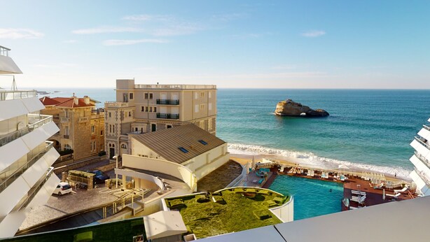 A coastal hotel with a pool, a rocky outcrop in the sea, and a view of the ocean. - Studio Roche Ronde - Welkeys (Biarritz)