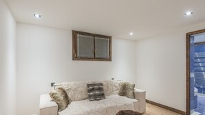 En moderne stue med sofa, to bløde skamler og et vindue med rullegardiner.