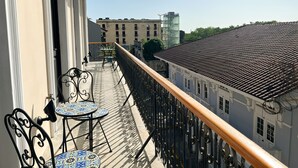 Un balcón con una mesa y sillas, barandilla y vista de edificios al fondo.