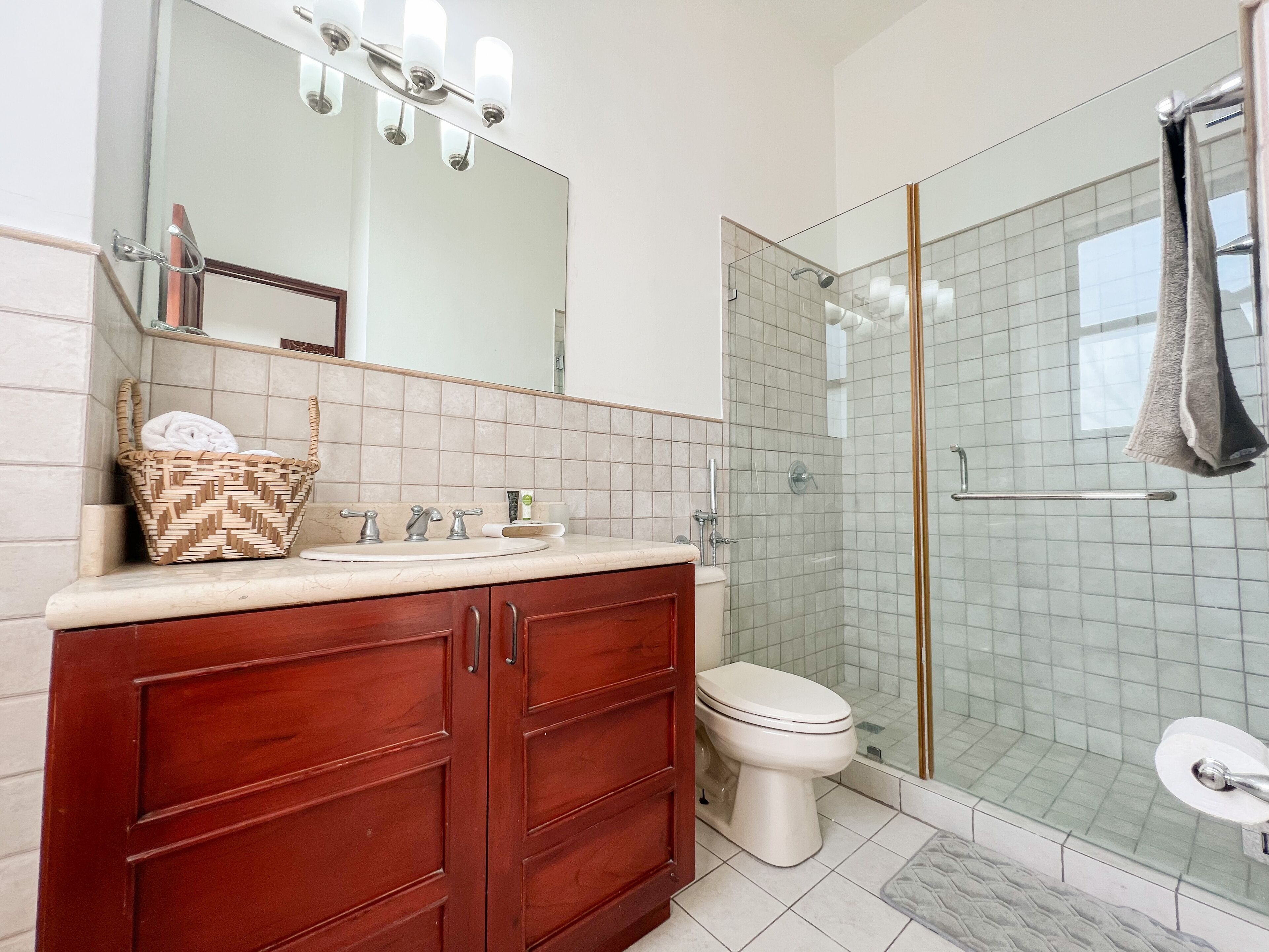 A bathroom with a wooden vanity, a white sink, a mirror, a glass shower enclosure, and a toilet.