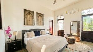 Un dormitorio con cama, mesitas de noche, ventilador de techo, ventana con vistas y detalles decorativos.