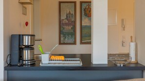 A kitchen with a coffee maker, a kettle, and a dish rack. There are two framed paintings on the wall.